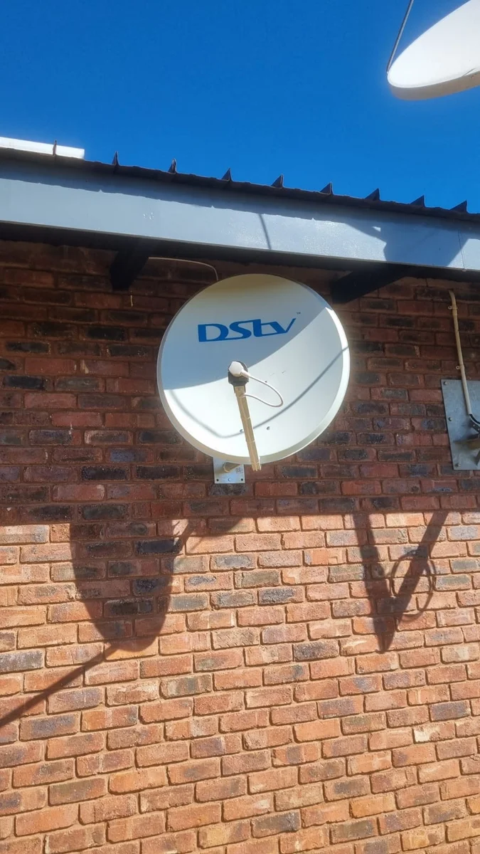 Wall-mounted DStv satellite dish being checked for signal problems