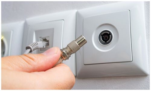 A coaxial connector being plugged into a wall-mounted TV point
